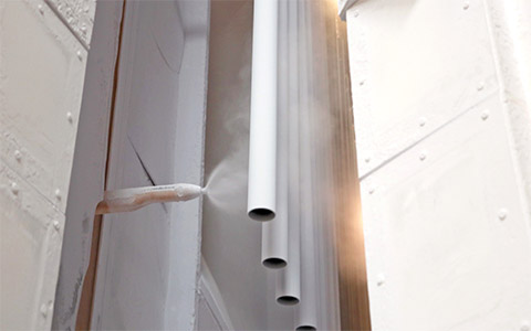 壁から静電スプレーガンが見えています。スプレーガンから列になった標識柱に順に塗料が噴射されています。